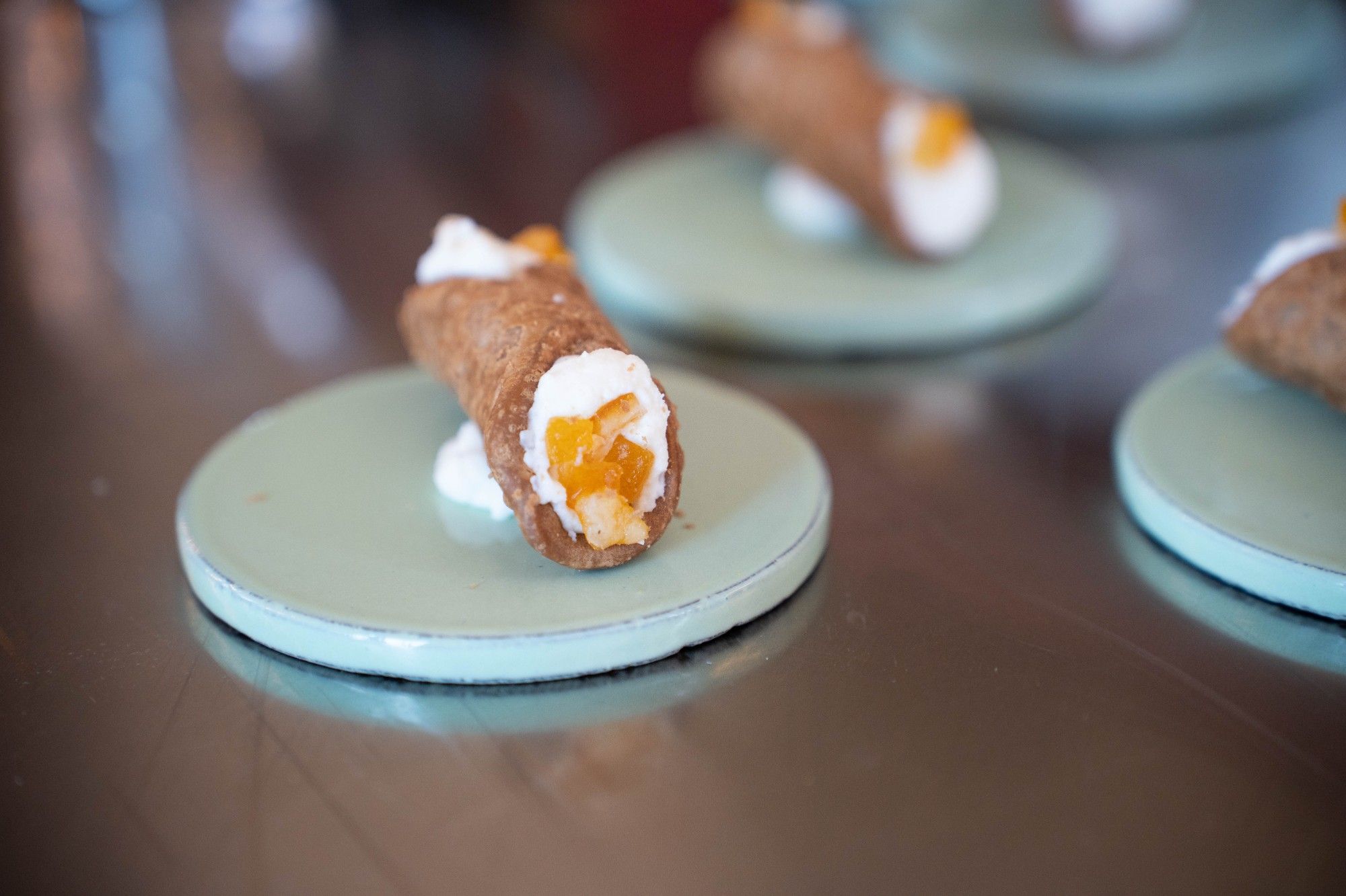 Cannolo siciliano con ricotta e arancia candita su un piattino di ceramica verde